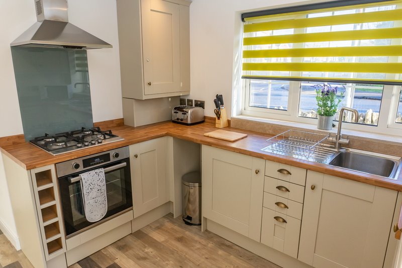 Modern kitchen with cream cabinets, wooden countertops, gas hob and yellow striped blind