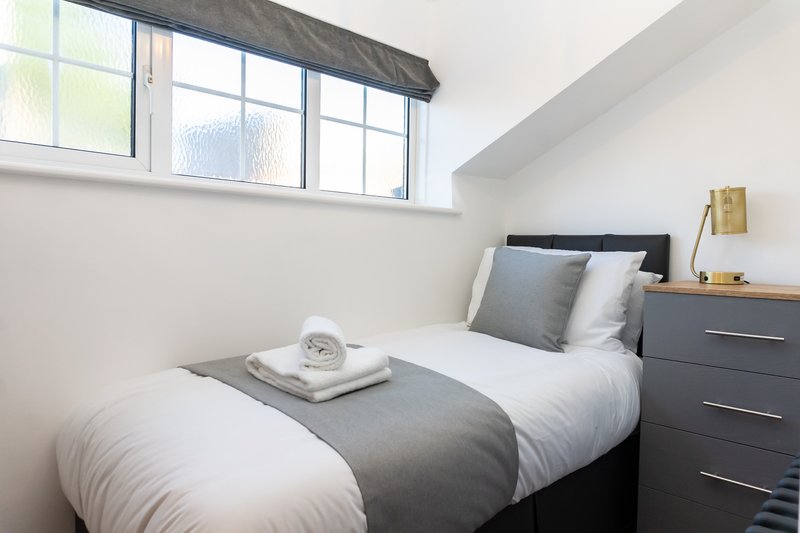 Modern bedroom with single bed, grey headboard, dark dresser and high window