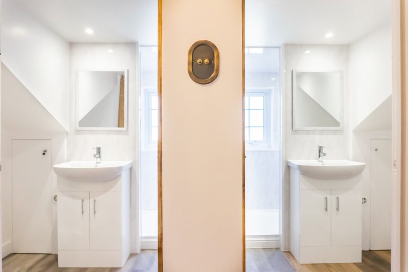 Dual bathroom setup with matching white vanities, mirrors, and warm peach-toned dividing wall