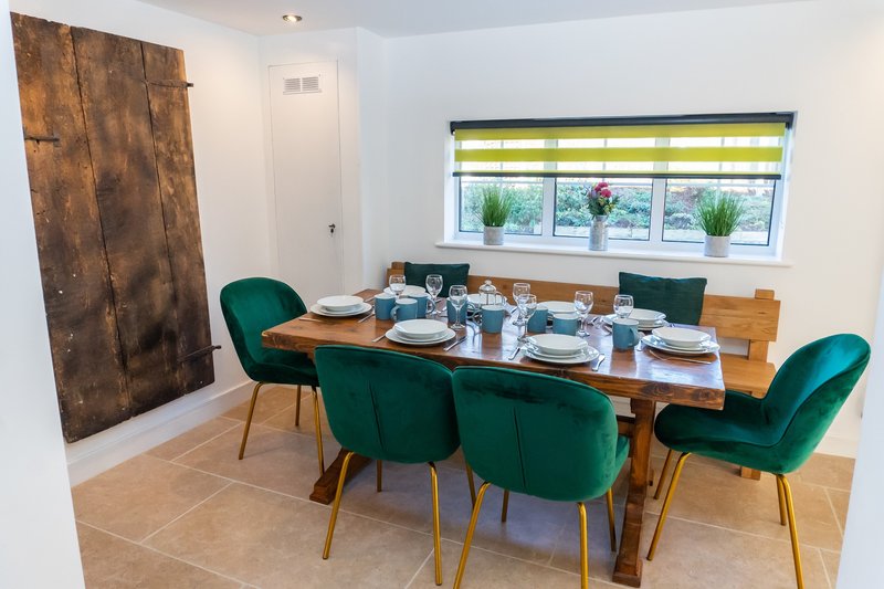 Modern dining room with wooden table, teal velvet chairs, place settings and window view