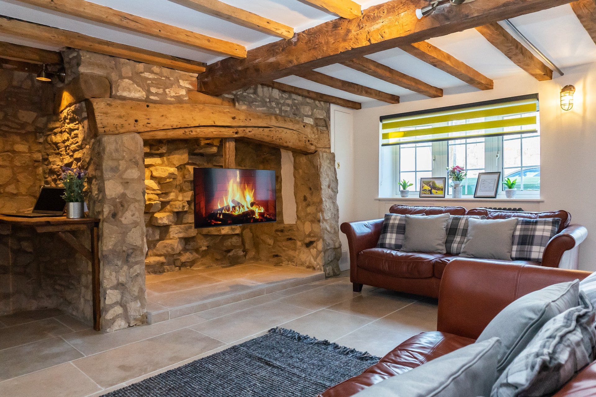 Rustic living room with stone fireplace, exposed beams, leather sofa and window