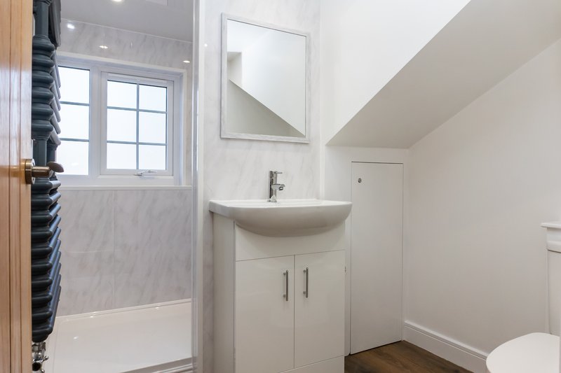 Modern bathroom with white vanity sink, mirror, toilet, and shower enclosure with window