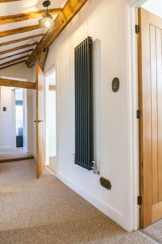 Hallway with exposed wooden beams, white walls, vertical radiator and wooden doors