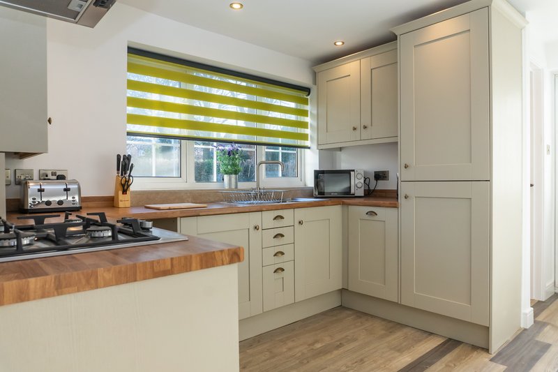 Modern kitchen with cream cabinets, wooden countertops, gas hob and striped window blind