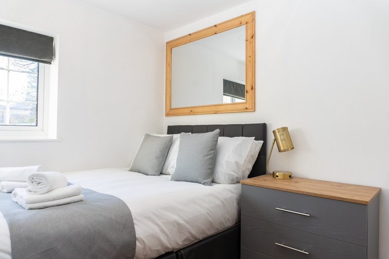 Modern bedroom with double bed, grey headboard, wooden mirror and bedside table