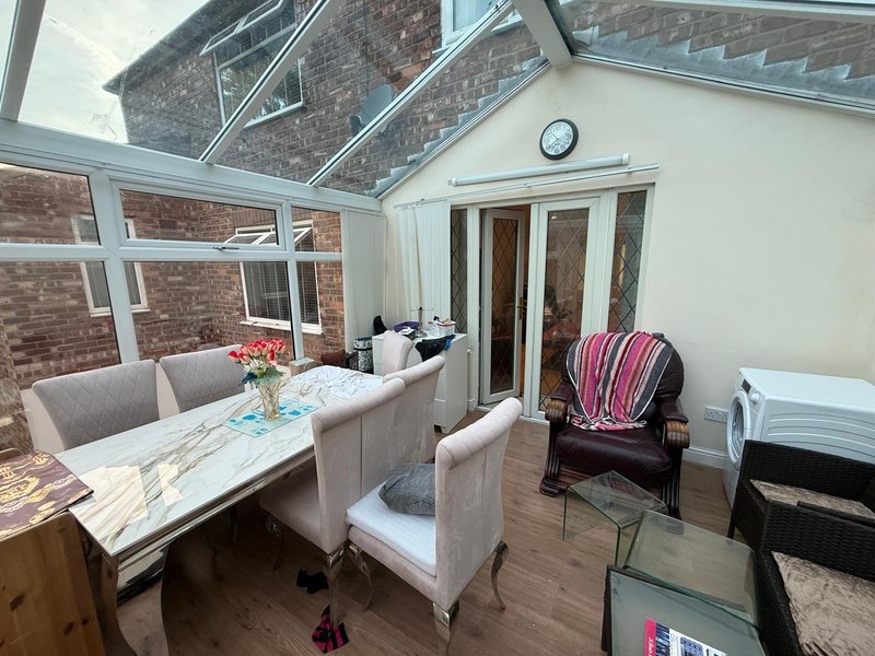 Bright conservatory with dining table, upholstered chairs, glass roof and brick exterior walls
