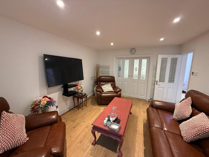 Spacious living room with brown leather sofas, red ottoman, wall-mounted TV, and wooden flooring