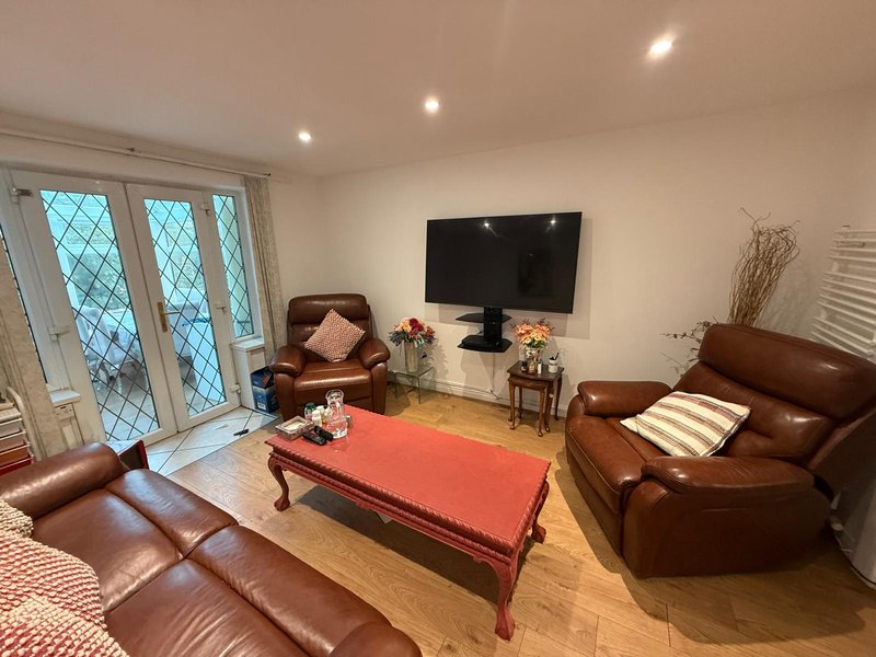 Living room with brown leather furniture, red ottoman, flat-screen TV, and French doors with latticed windows