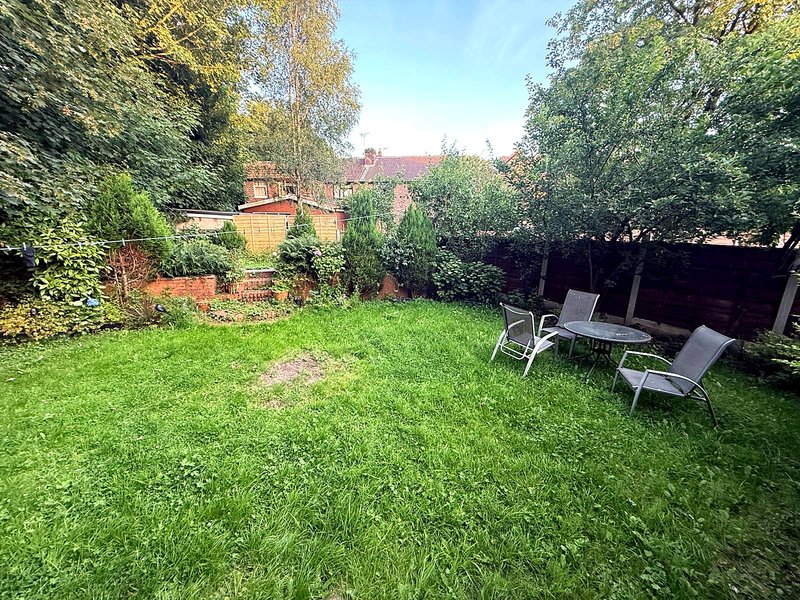 Garden with lawn, seating area, brick structures, and surrounding trees and hedges