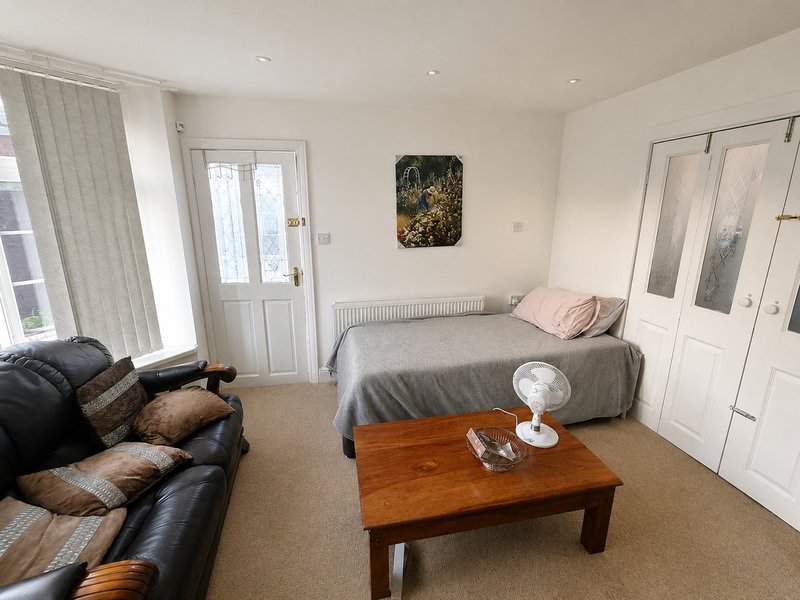 Studio bedroom with double bed, black leather sofa, wooden coffee table and glass doors