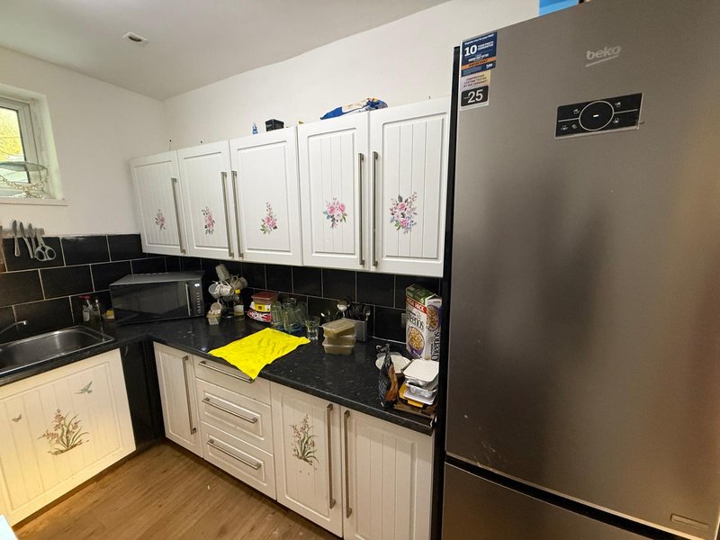 Kitchen with cream cabinets, black countertop, stainless steel fridge, and black tile backsplash