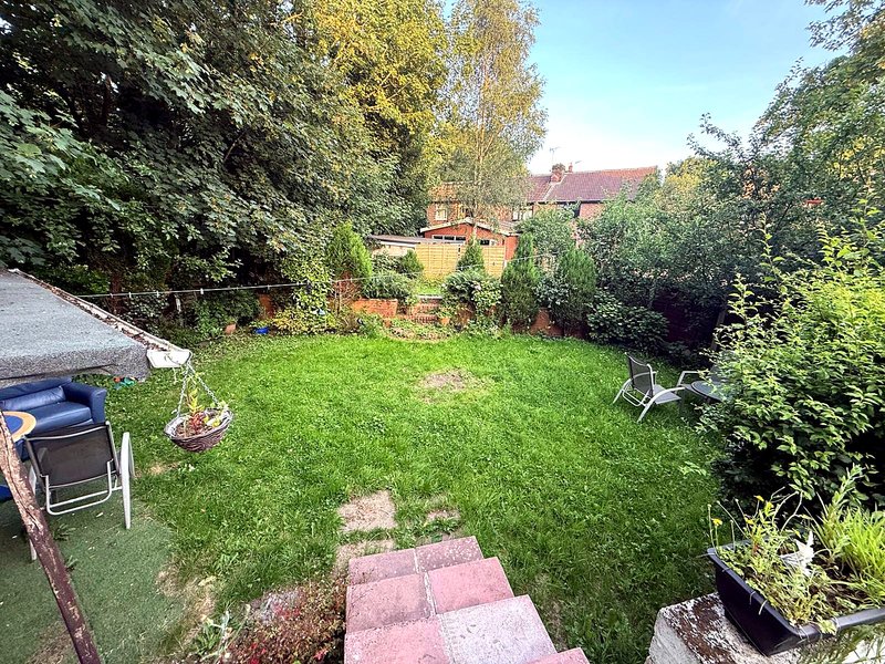 Garden with lawn, stepping stones, seating area, and surrounding hedges and trees