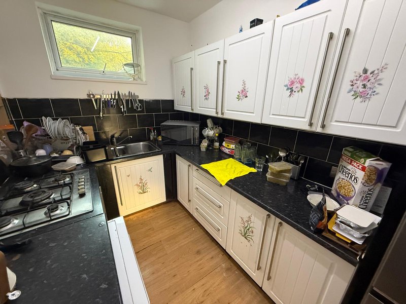 Kitchen with cream cabinets, black countertop, black tile backsplash and wooden flooring