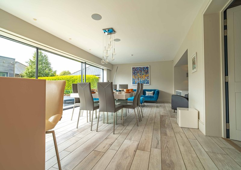Open-plan dining and living area with blue armchair, wooden flooring, large windows and garden views
