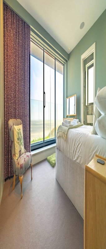 Bedroom with double bed, large windows, green walls, wooden furniture and towel rail
