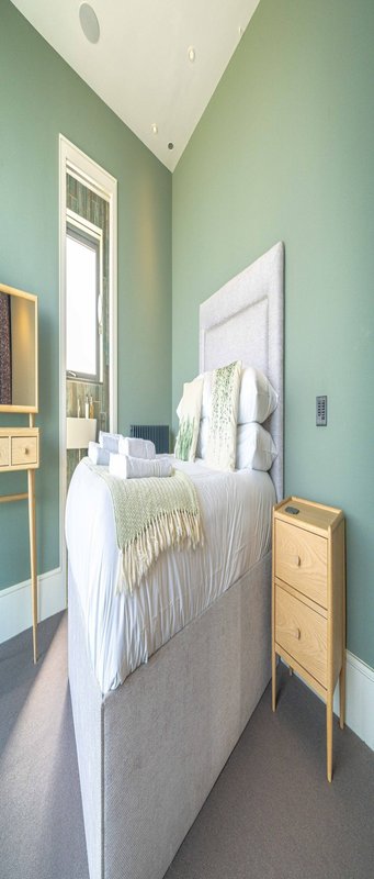 Bedroom with sage green walls, single bed with white bedding, wooden nightstands and natural light from window