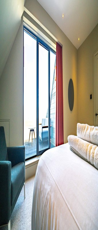 Modern bedroom with bed, armchair, floor-to-ceiling window with red curtains and city view