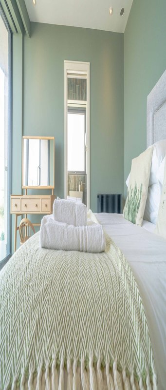 Narrow bedroom with sage-green walls, single bed, wooden dresser, and full-length mirror
