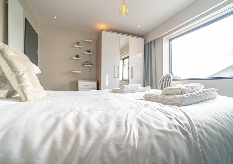 Modern bedroom with white bedding, built-in wardrobe, floating shelves and large window