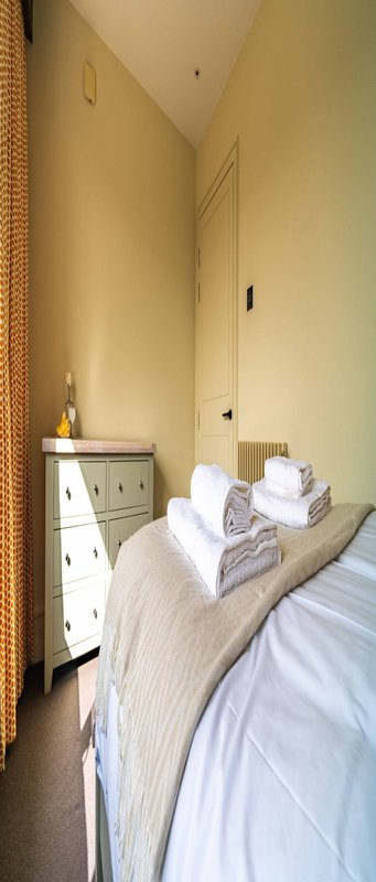 Narrow bedroom with single bed, white pillows, storage cabinet, and brick wall detail