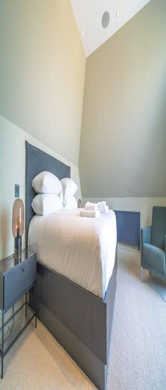 Modern bedroom with double bed, white pillows, bedside tables, and angled ceiling