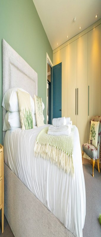 Modern bedroom with white bed, green accent wall, yellow wardrobe doors and recessed lighting