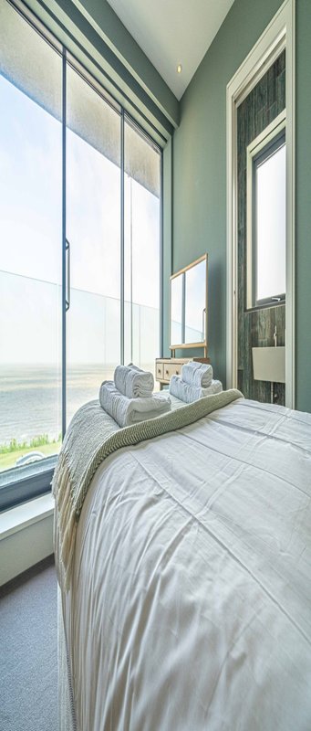 Bedroom with double bed, large windows overlooking water, modern green walls and white bedding