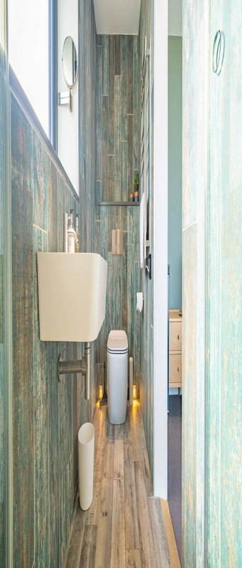 Narrow bathroom with teal tile walls, wooden floor, wall-mounted sink and toilet