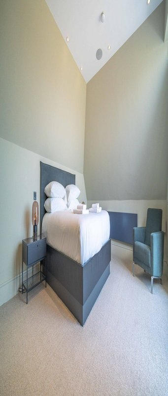 Modern bedroom with single bed, dark headboard, cream bedding, and angled ceiling