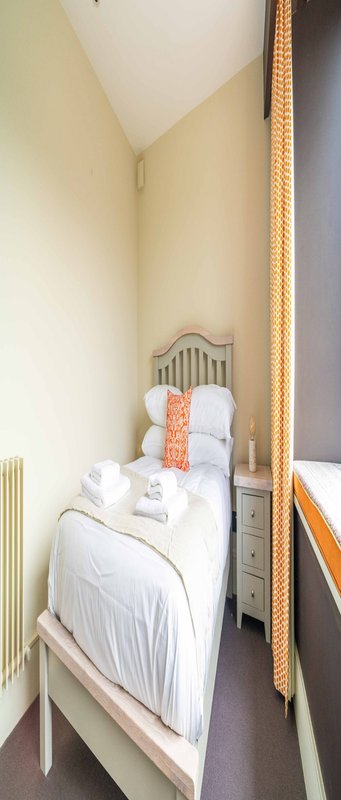 Narrow bedroom with single bed, white bedding, metal headboard and small nightstand