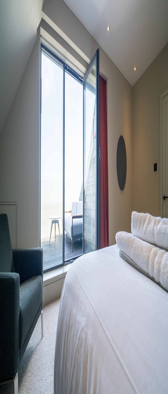 Modern bedroom with double bed, floor-to-ceiling windows, red curtains and armchair