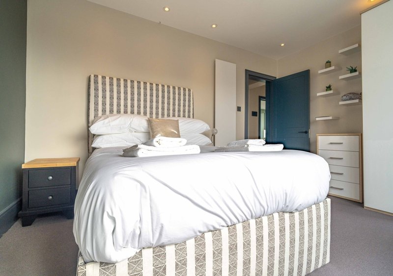 Modern bedroom with striped upholstered bed, white bedding, dark nightstand, and built-in storage