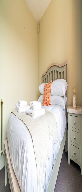Small bedroom with single bed, white bedding, metal headboard and wooden nightstand