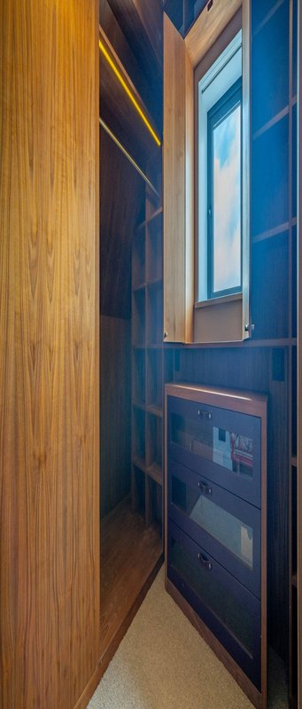 Narrow hallway with wooden door, blue wall paneling, window, and built-in storage drawers