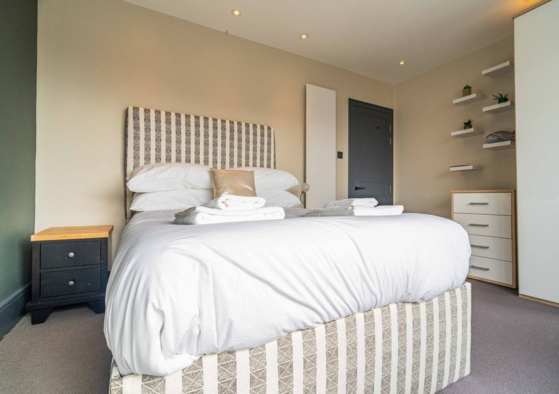 Modern bedroom with striped bed frame, white bedding, dark bedside table, and fitted storage shelving