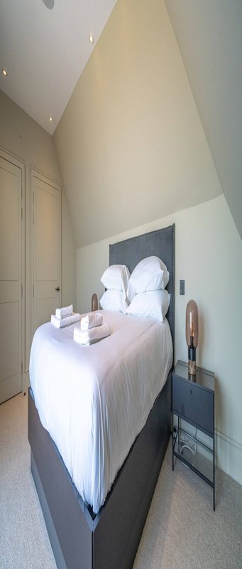 Narrow bedroom with single bed, white bedding, pillows, and wall-mounted headboard feature