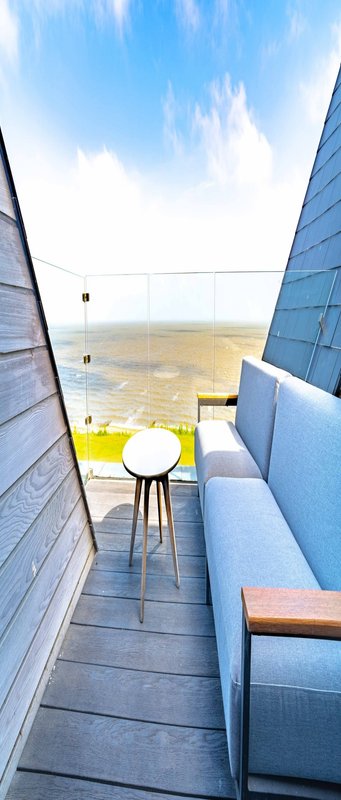 Modern minimalist interior with yellow chair, white table, and coastal view through opening