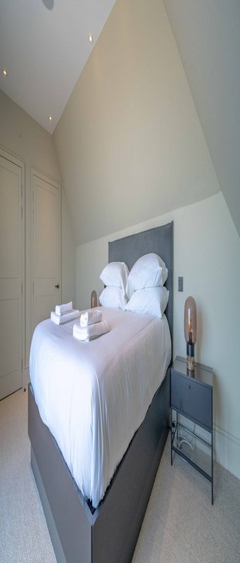 Modern bedroom with double bed, white bedding, pillows, and small side table