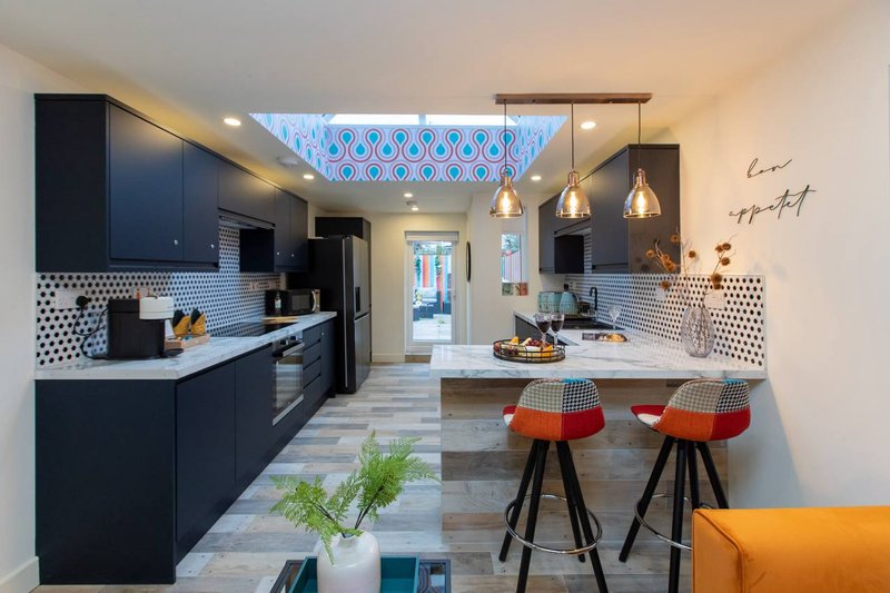 Modern open-plan kitchen with dark cabinetry, white countertop, island seating, pendant lighting