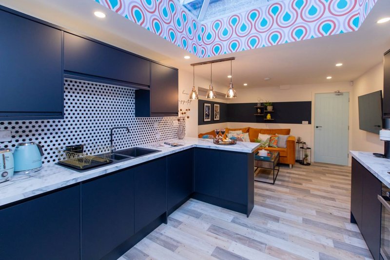 Modern kitchen with dark blue cabinetry, white countertops, geometric ceiling feature, and open-plan living area