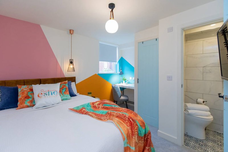 Colorful modern bedroom with double bed, pink accent wall, and ensuite bathroom visible