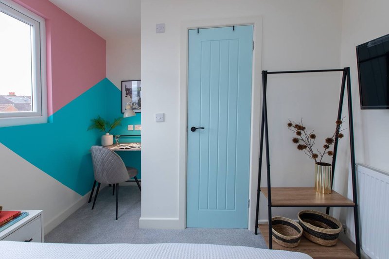 Modern bedroom with geometric pink and teal accent walls, desk area, and minimalist furnishings