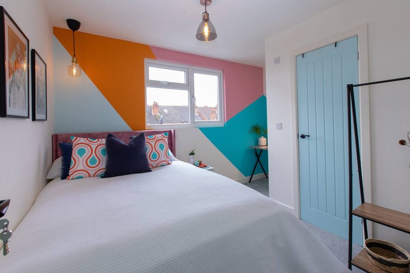 Bright modern bedroom with colorful geometric wall paint, double bed and patterned cushions