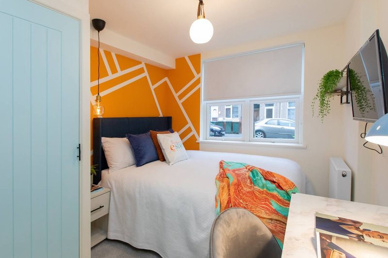 Modern bedroom with orange geometric accent wall, double bed with navy headboard and white bedding