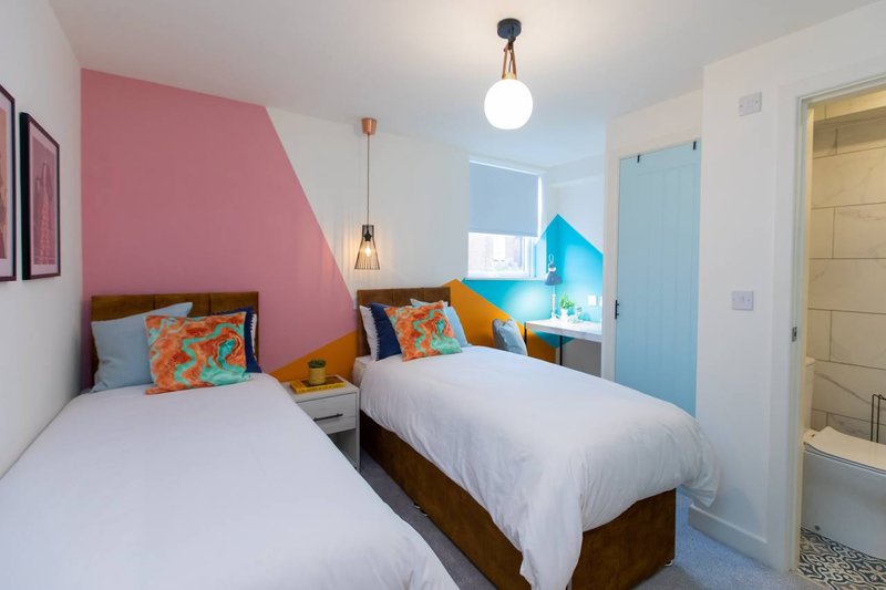 Bright bedroom with two single beds, pink accent wall, colorful cushions and modern lighting