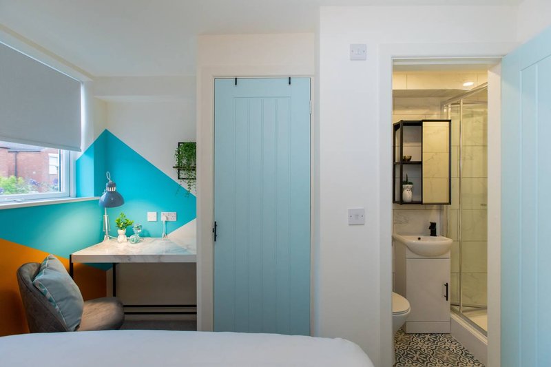 Bedroom with double bed, turquoise accent wall, desk nook, and ensuite bathroom visible