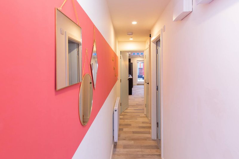 Modern hallway with pink and white walls, wooden flooring, and multiple doors
