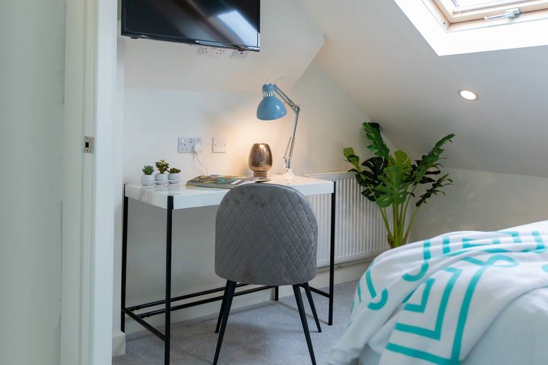 Modern bedroom with desk, chair, potted plant, TV and bed with turquoise bedding