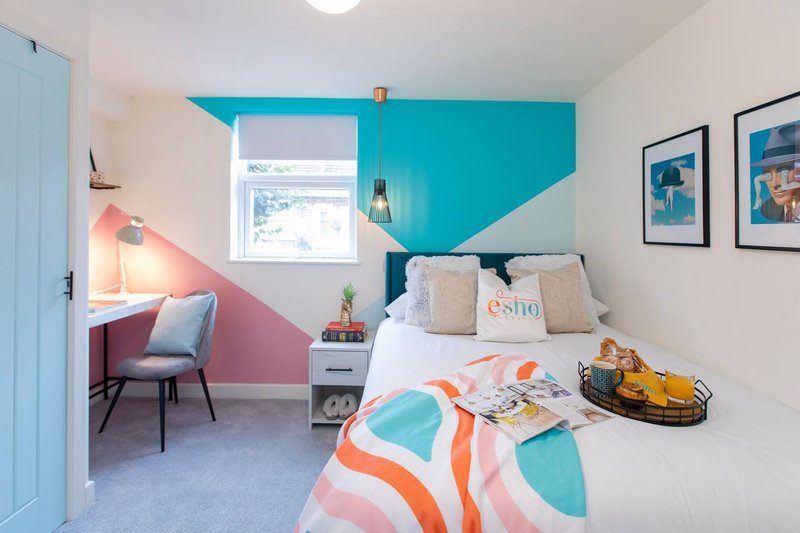 Modern bedroom with turquoise and pink accent walls, double bed, desk area, and framed artwork