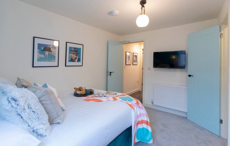 Bright bedroom with double bed, blue cushions, wall-mounted TV, and light blue door